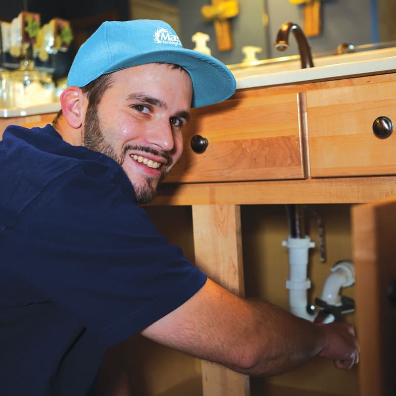Smiling plumber repairing pipes under a cabinet sink